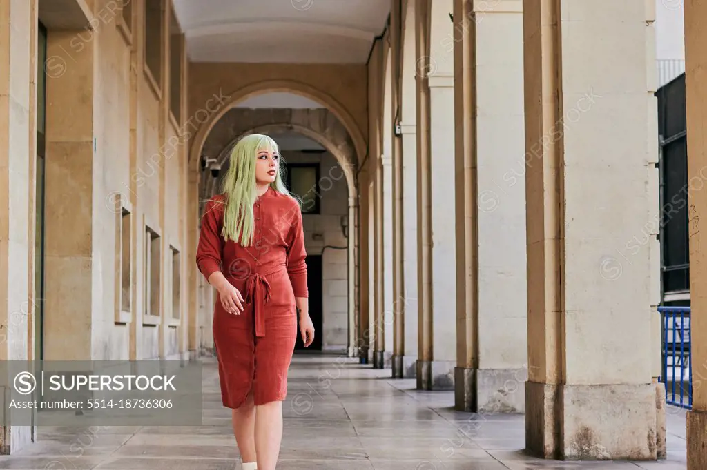 Alternative woman with green hair and red dress walks in old building
