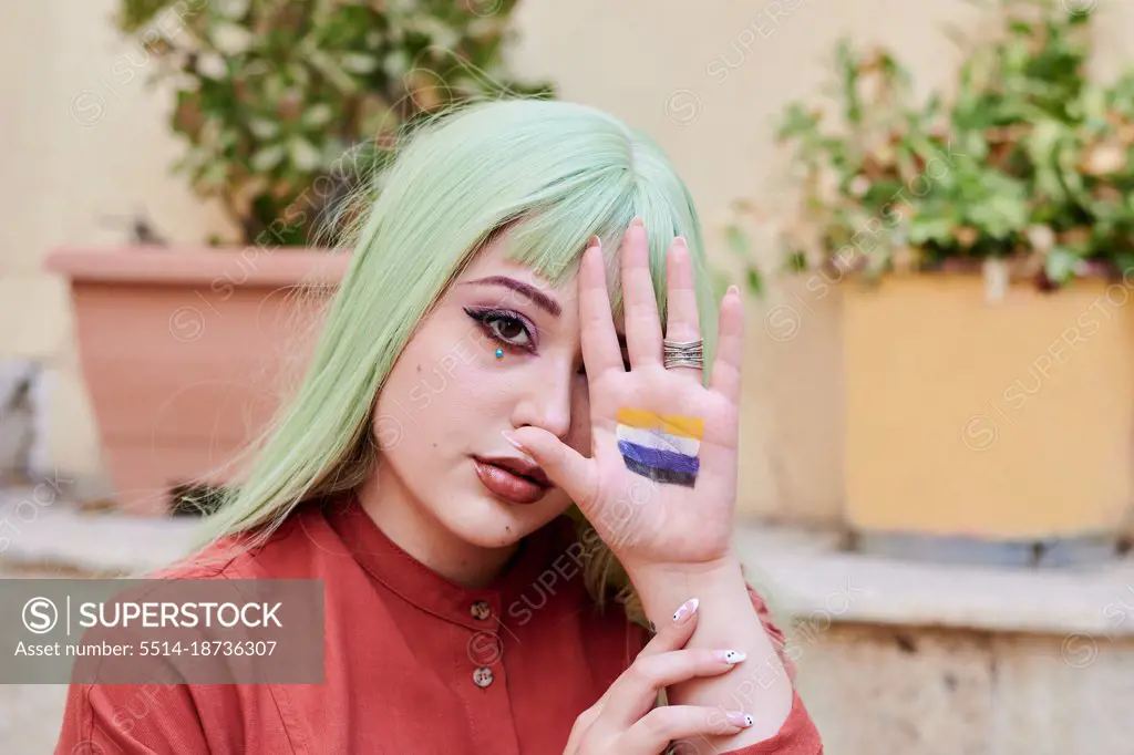 Person with green hair shows non-binary flag in the palm of her hand