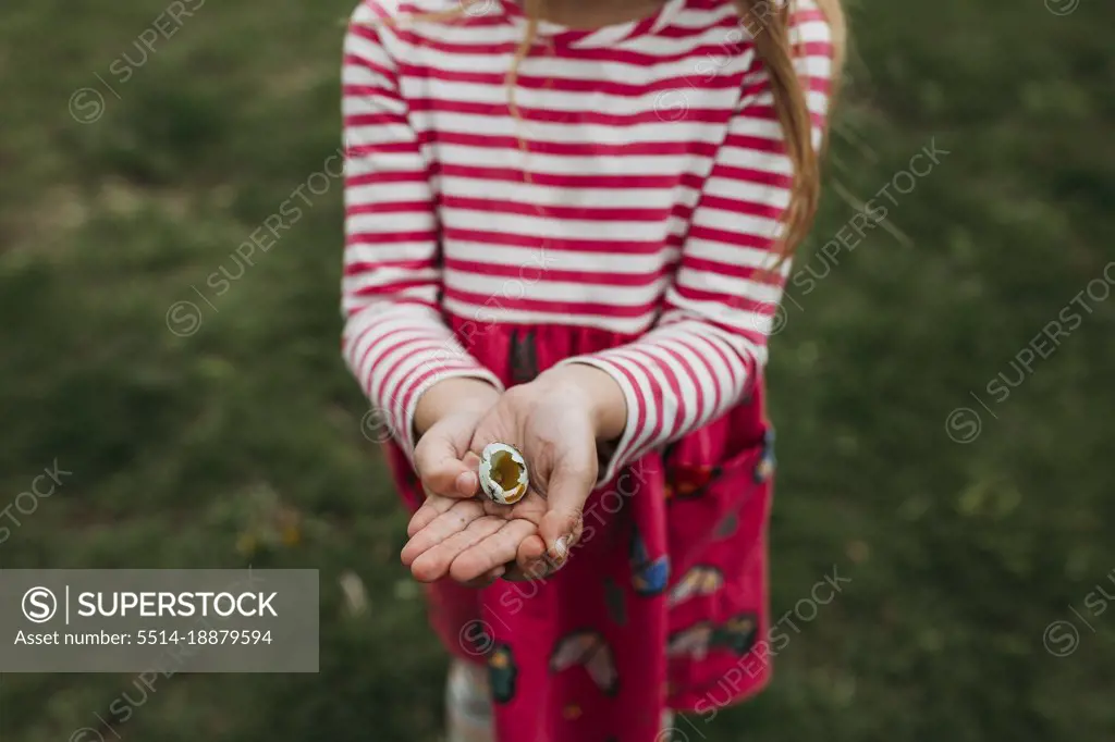 Girl holding broken robin's egg in palm of hand
