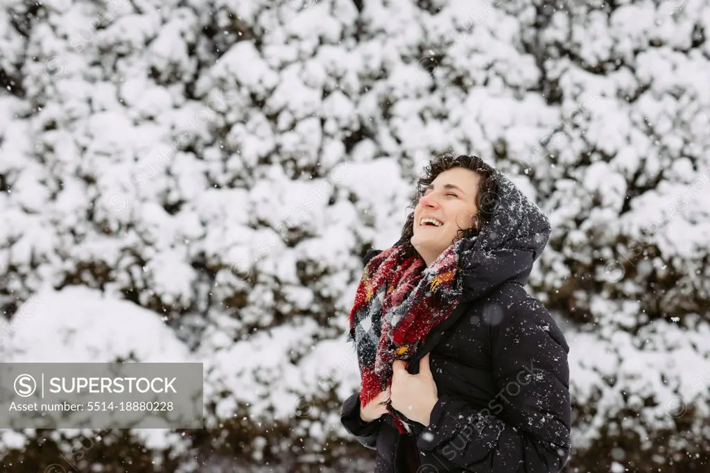 Woman in hood and red scarf smiling and laughing outside on snow