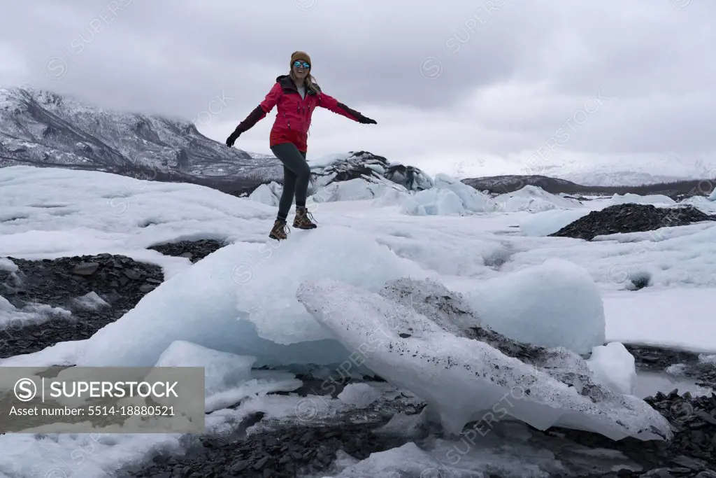 Adventurous woman with arms outstretched standing on ice formation