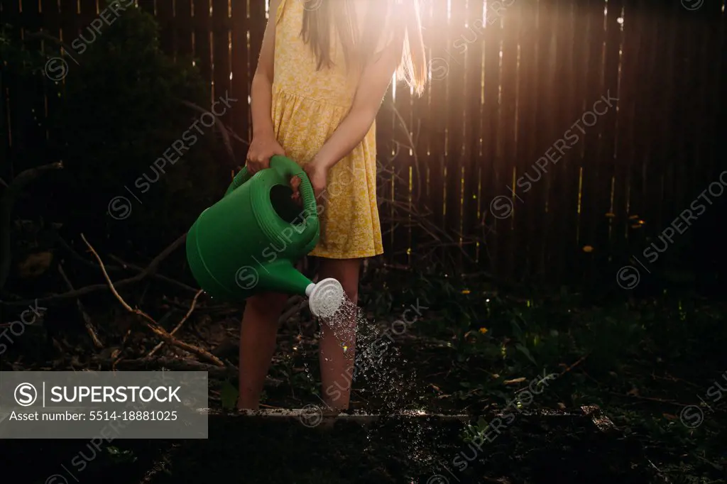 Young girl watering garden plot with watering can