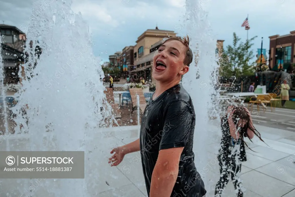Happy Teen Boy playing in fountains on summer day