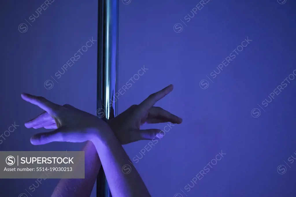 Detail of female athlete's hands posed on pole in pole dance studio