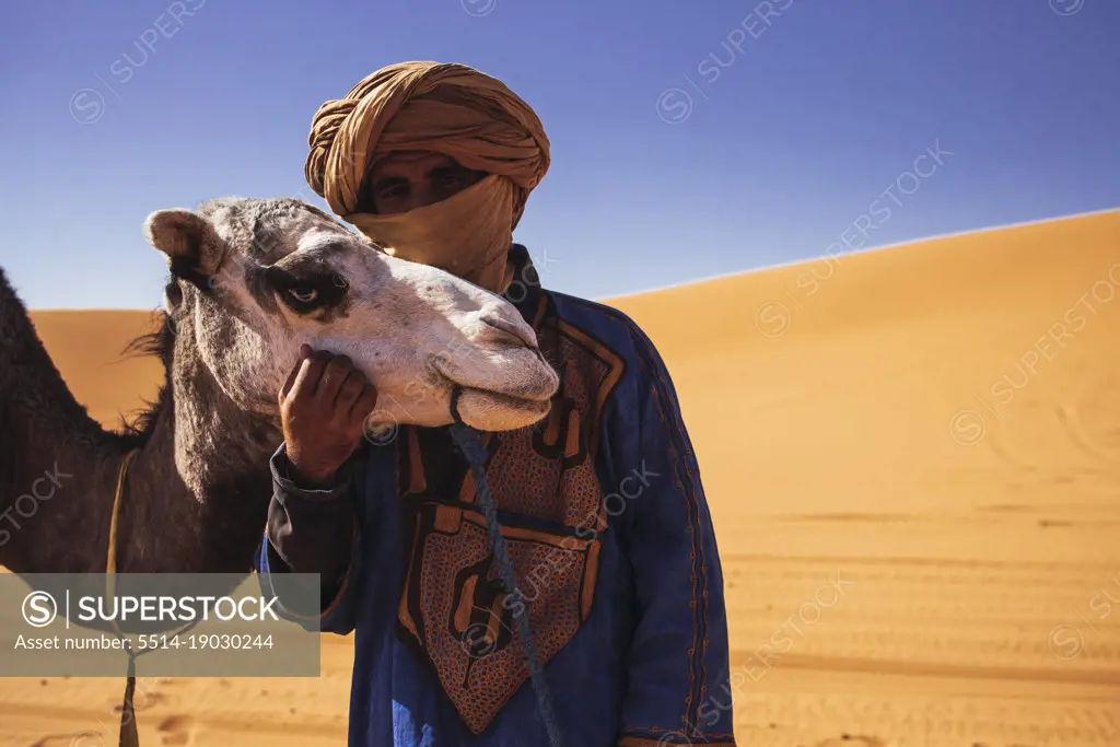 A Bereber guide hugging his camel in Merzouga desert, Morocco.