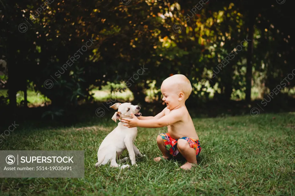 Adorable smiling toddler about to hug a white puppy in summer