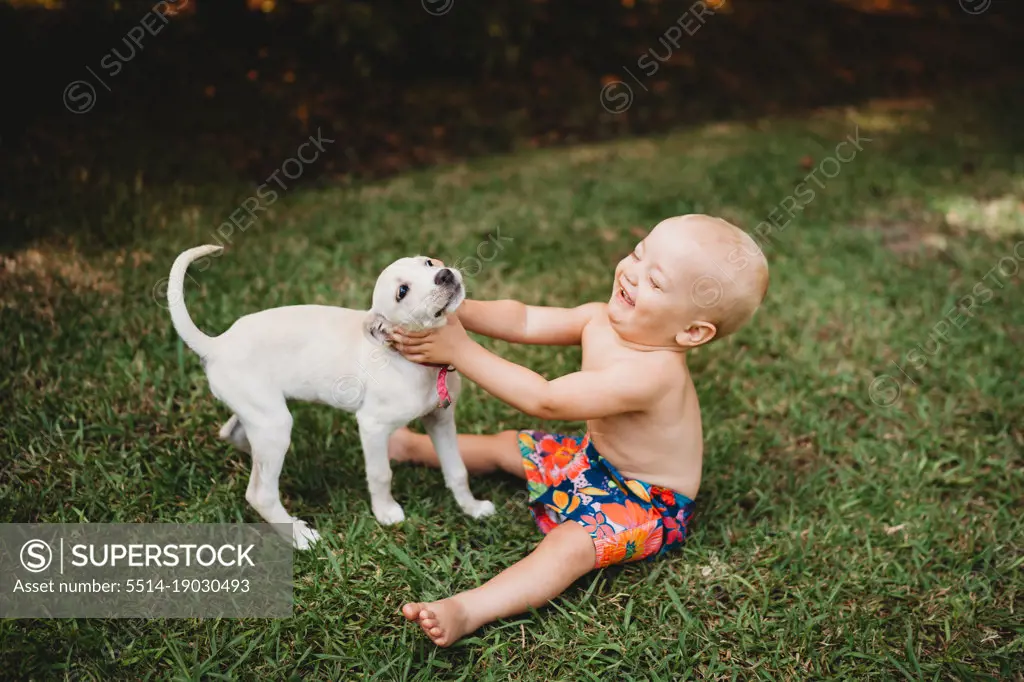 Happy baby laughing with a beautiful puppy outside in summer