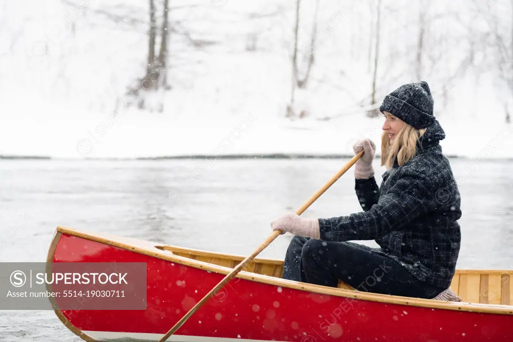 Portrait of an excited woman rowing a canoe on a snowy river.