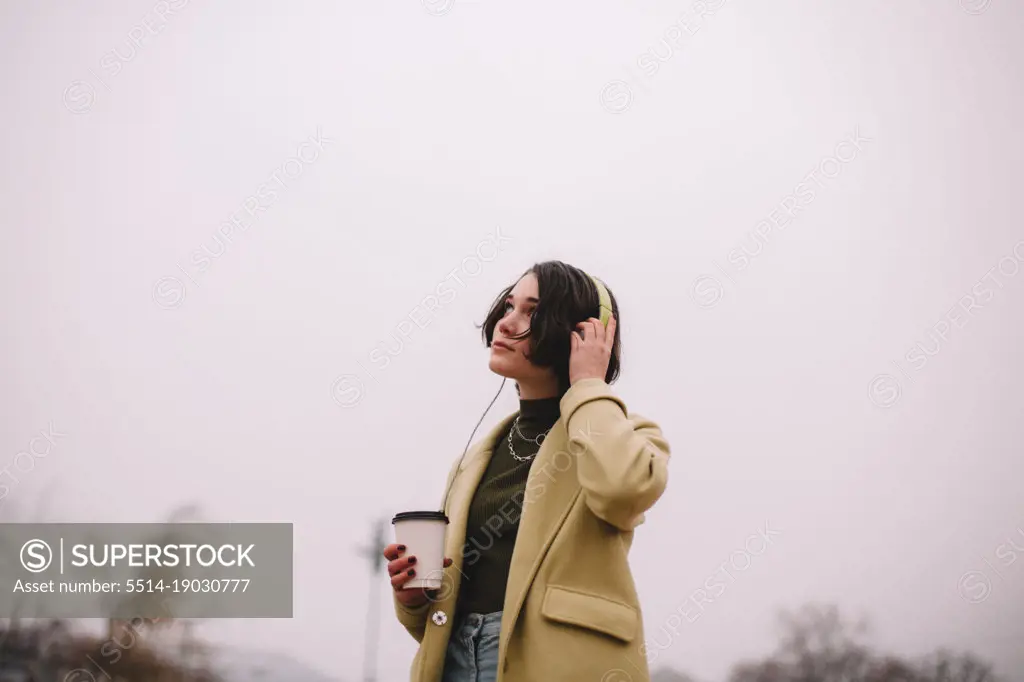 Thoughtful young woman listening music in headphones walking in city