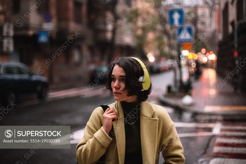 Thoughtful young woman in headphones standing on street in city