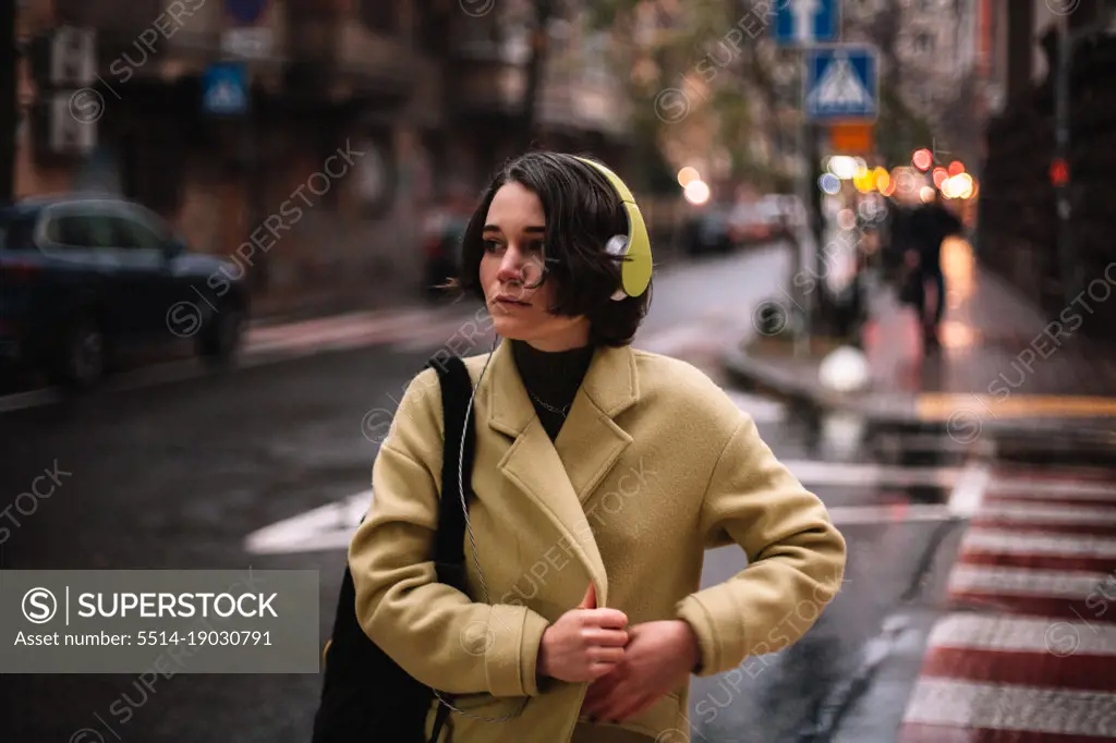 Thoughtful young woman in headphones walking on street in city
