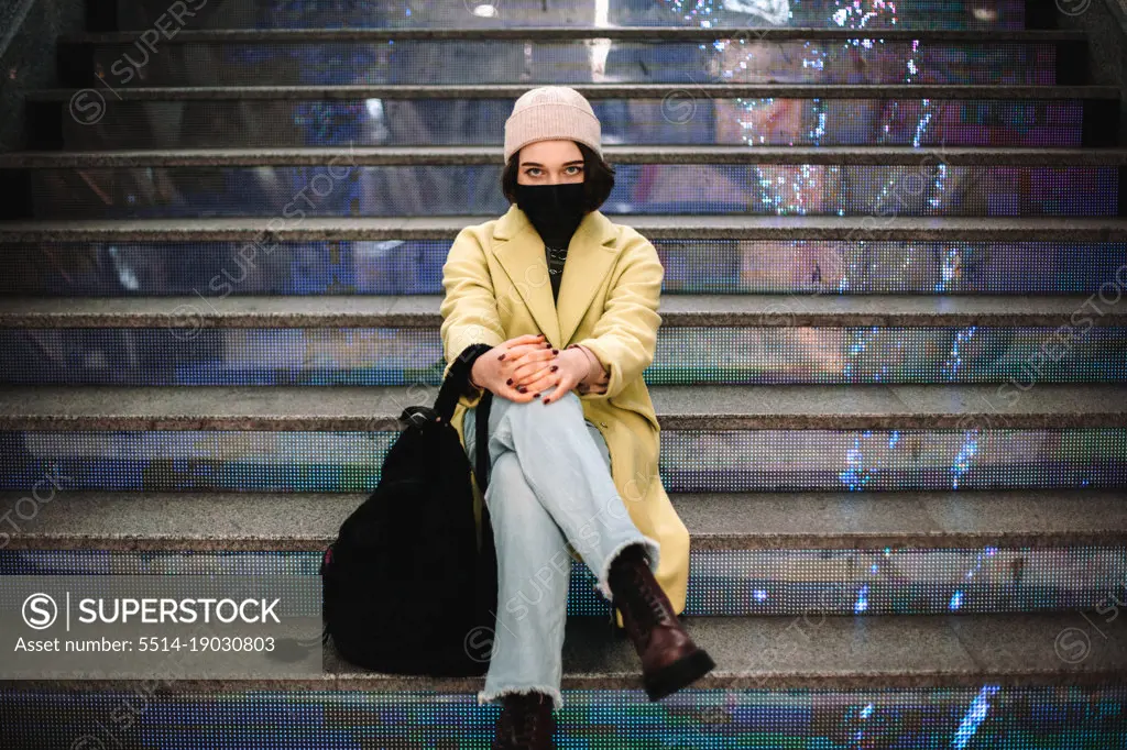 Portrait of confident young woman wearing face mask sitting on steps