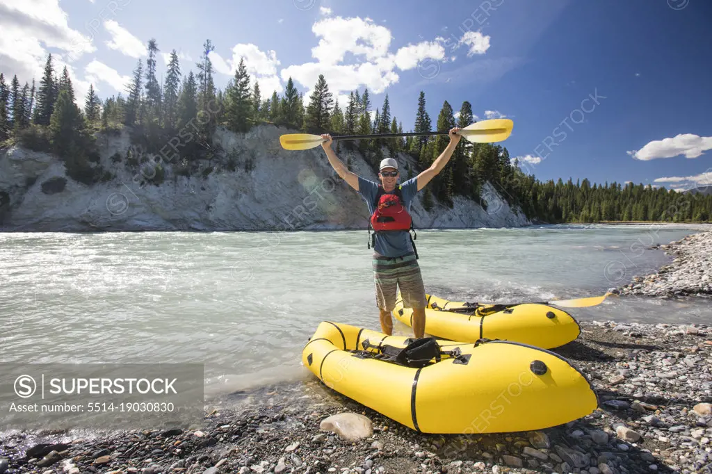 Paddler holds yellow paddle above head while rafting