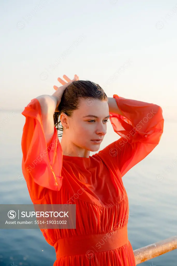 a woman in a wet red dress with wet hair stands near the blue water