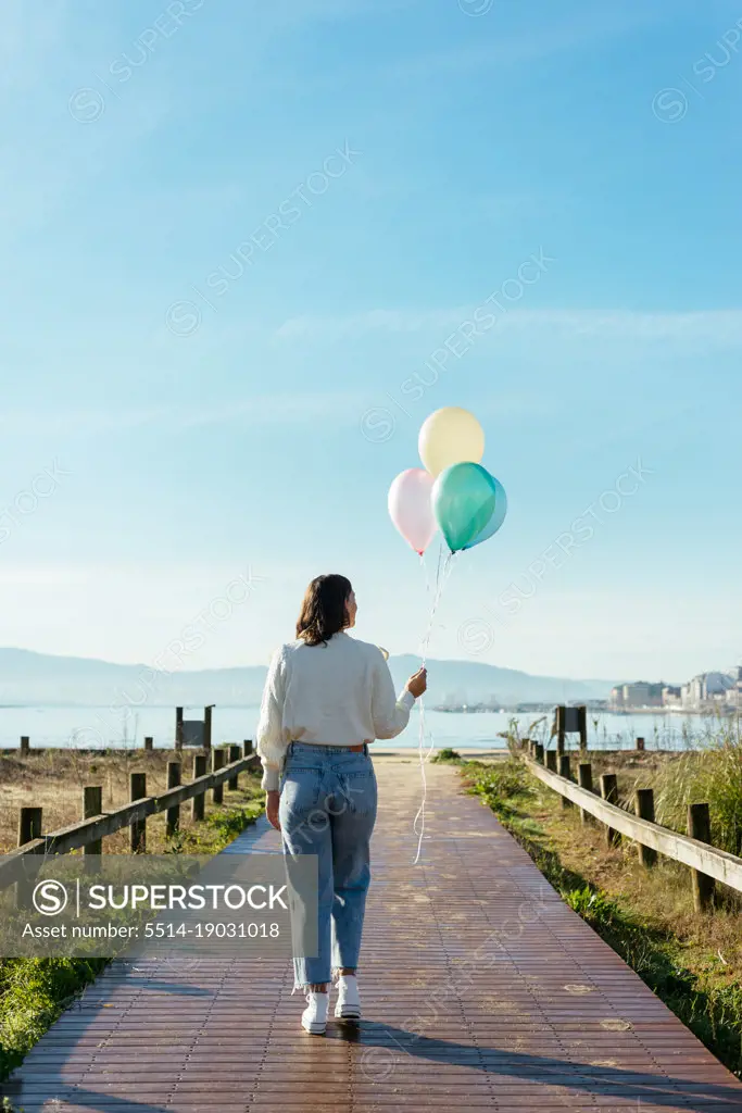 Anonymous Woman With Balloons Walking Over A Footbridge