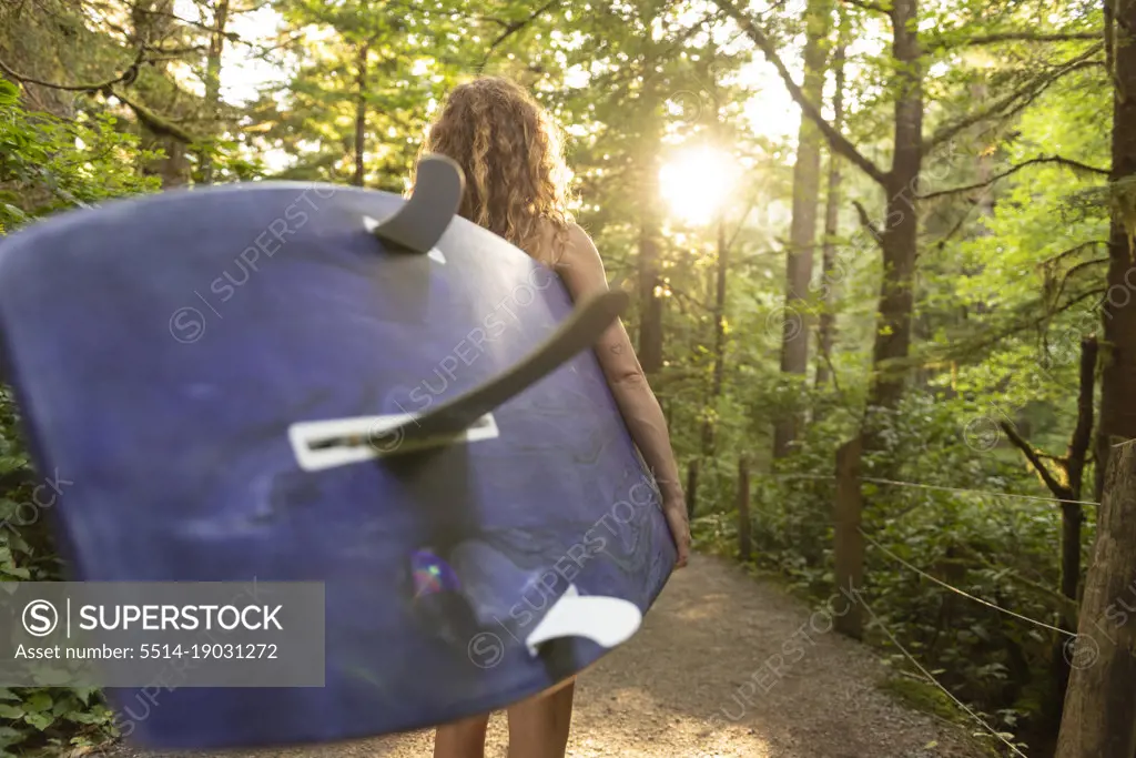 Woman carrying surfboard down trail to the ocean