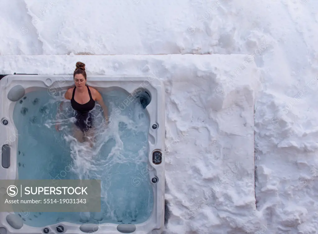 Overhead of woman relaxing in hot tub on snow covered deck in winter.