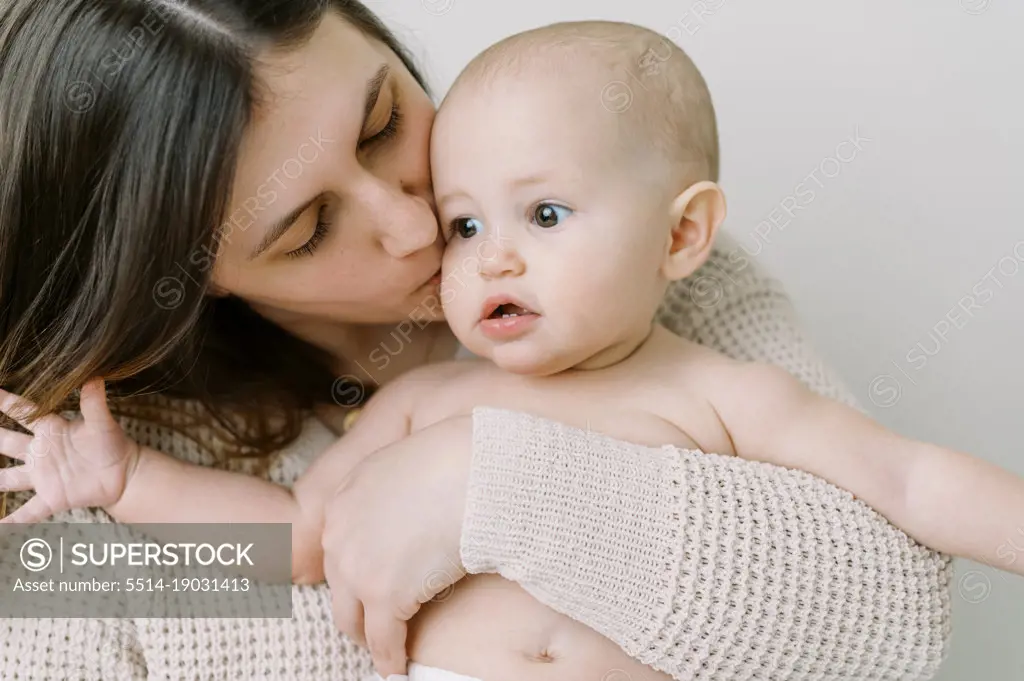 young mother holding her young baby daughter and kissing her