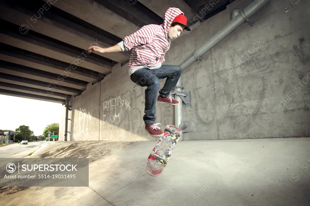 Young male skateboarding under overpass