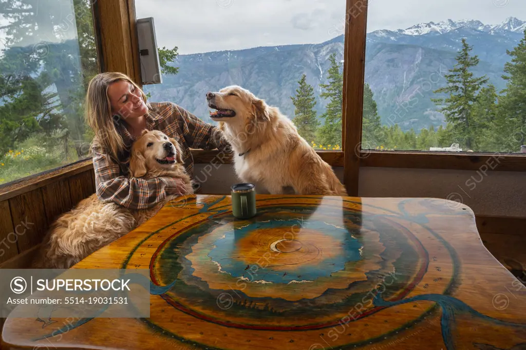 Happy female and dogs at the table in a mountain cabin