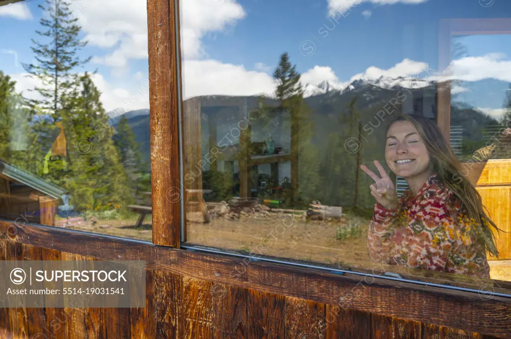 Female showing the peace sign through a mountain cabin window