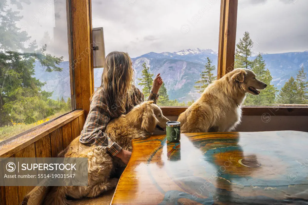 A female and their dogs sitting at the table in a mountain cabin