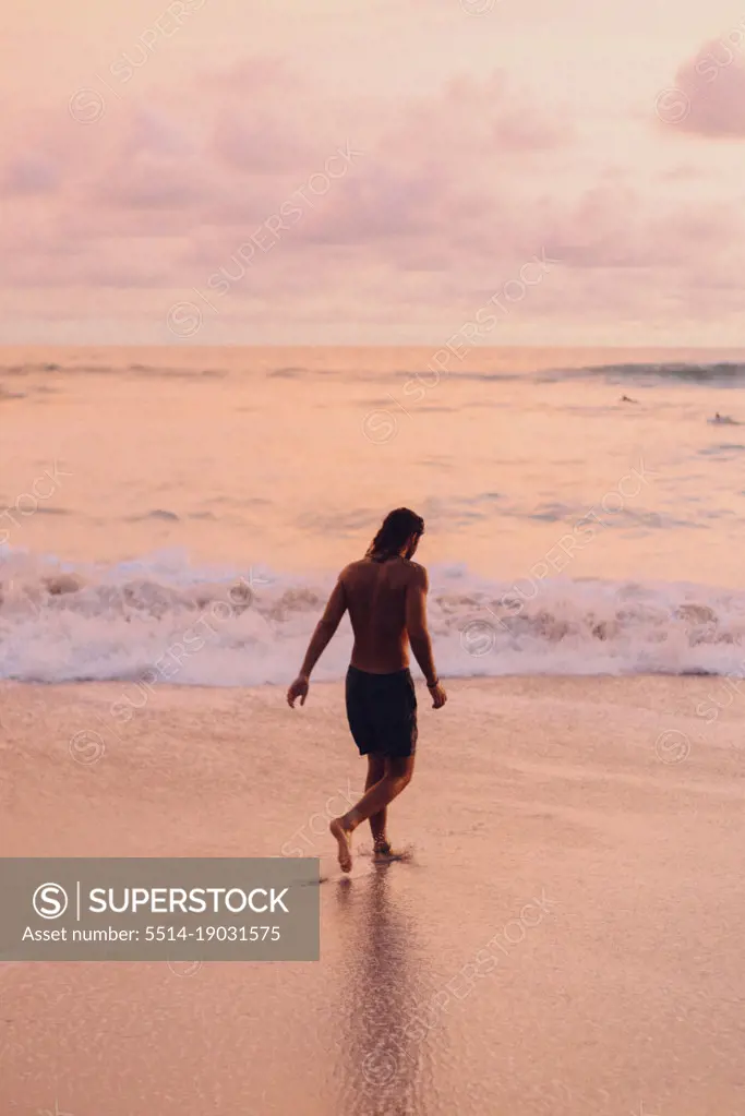 a surfer walking to the ocean during the sunset