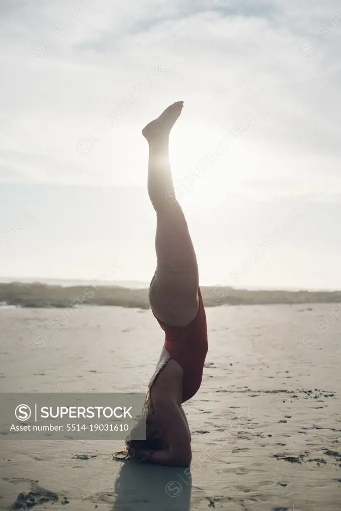 backlighting portrait of a blond girl making a yoga pose on the beach