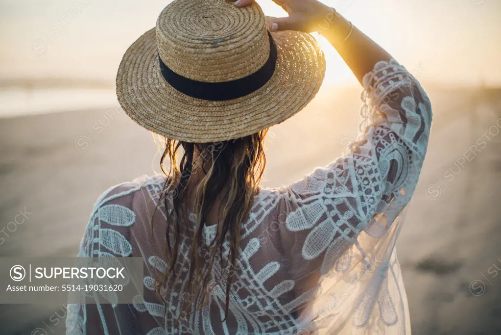 blond girl with a hat watching the sunset on the beach