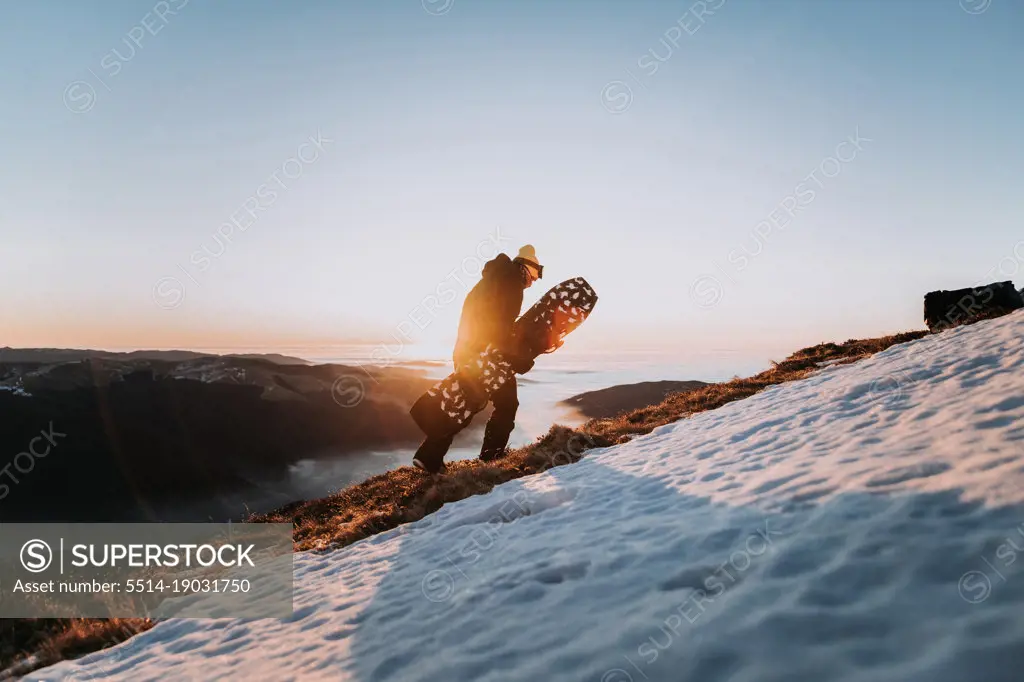 Snowboarder in sportswear hiking in the mountains with snowboard