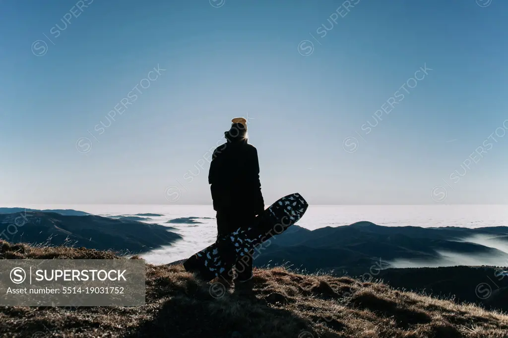 Silhouette of a snowboarder holding his snowboard on the mountain
