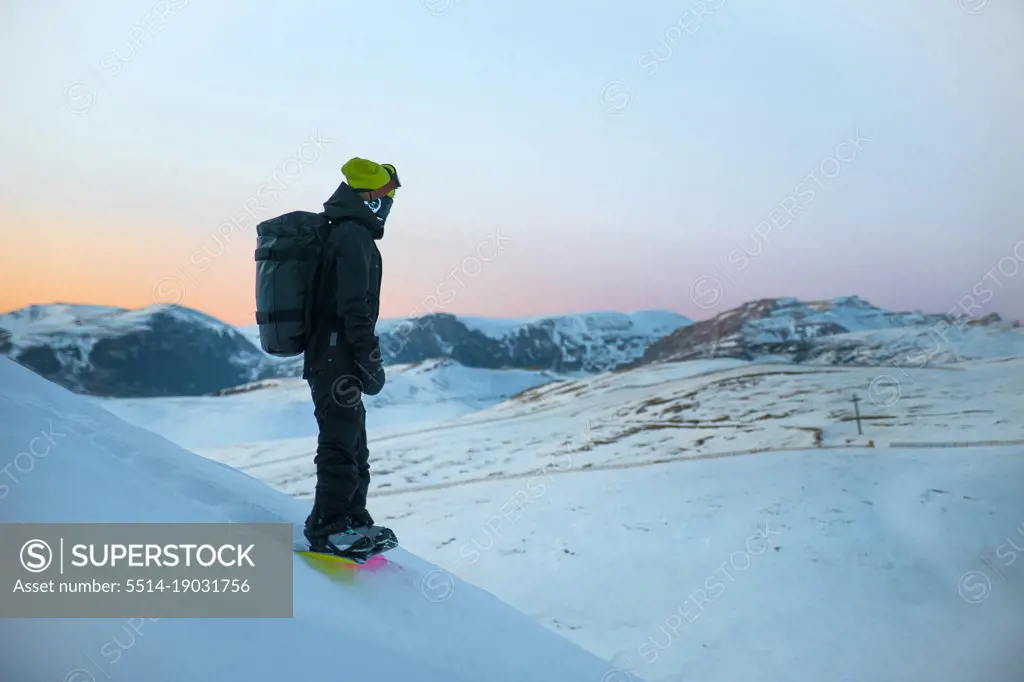 Athlete snowboarder with backpack enjoying the view at sunset