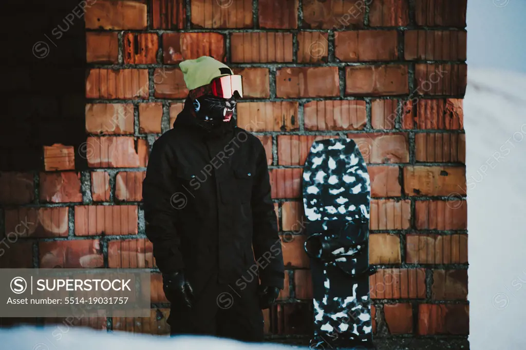 Snowboarder posing wearing snowsuit close to a brick wall