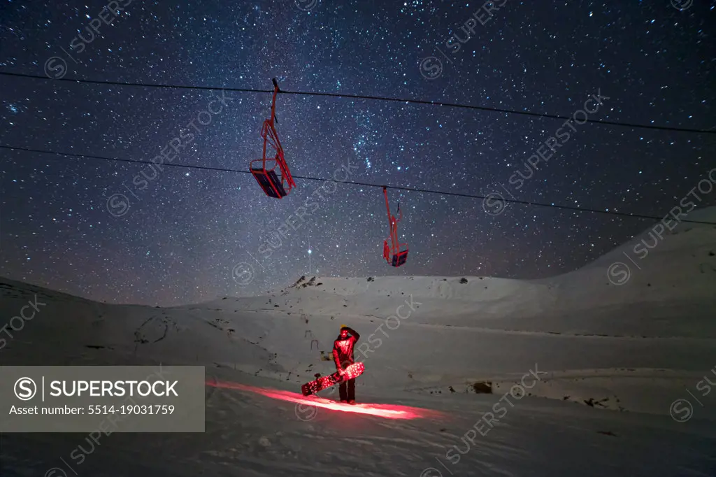 Snowboarder at night under the chairlift with sky full of stars