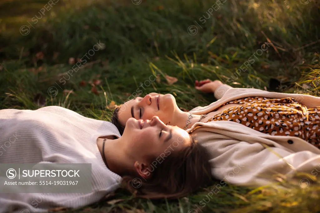 Happy lesbian couple smiling while lying on grass with eyes closed