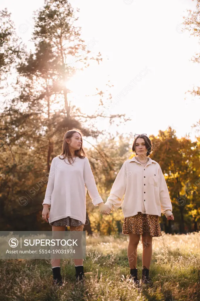 Lesbian couple holding hands while standing in forest during autumn