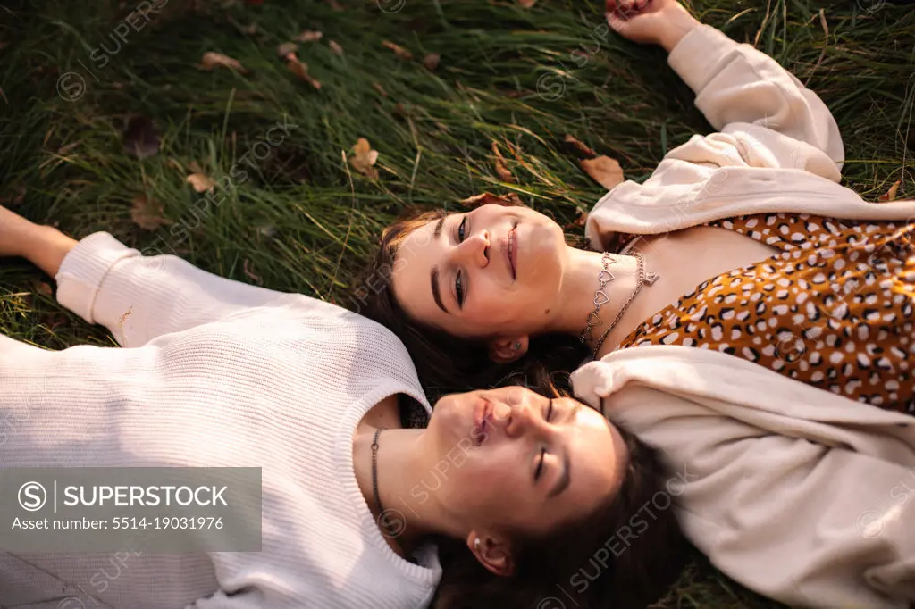 Two happy female friends smiling while lying on grass