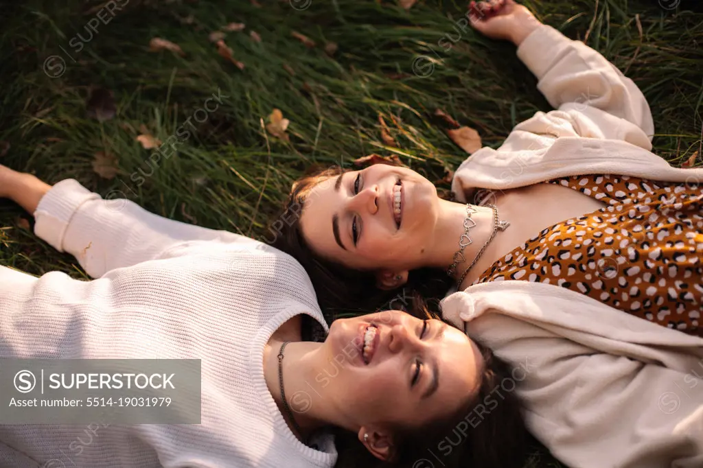 Two happy young women smiling while lying on grass
