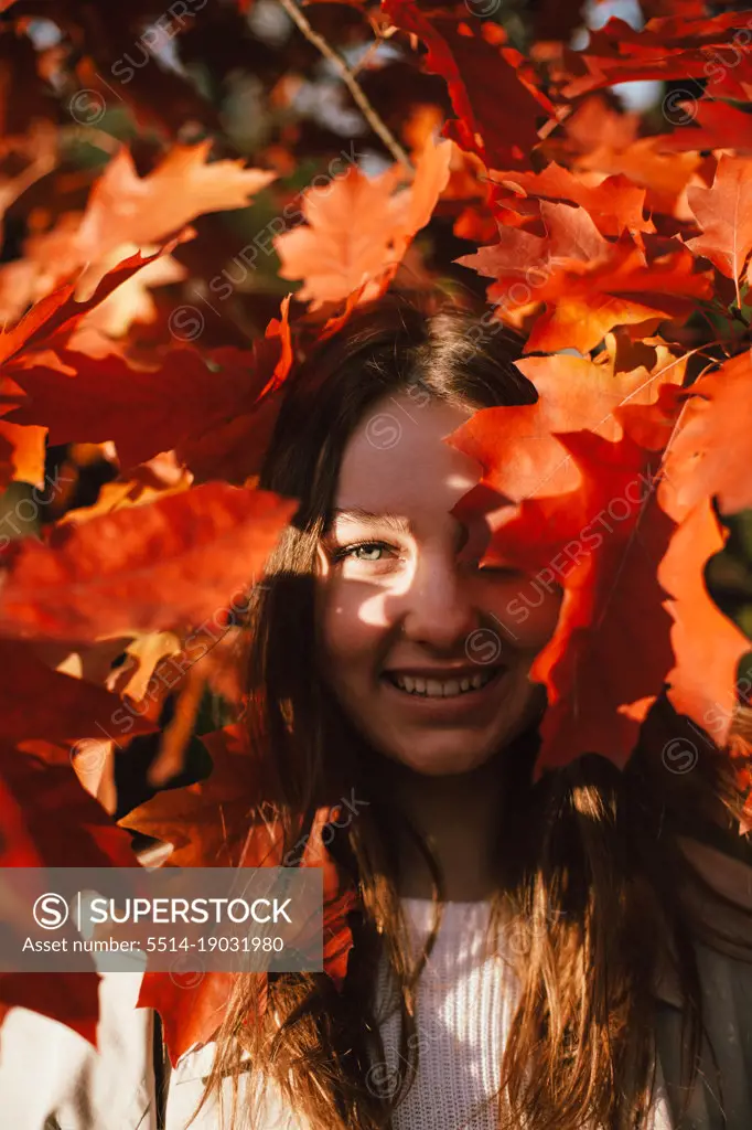 Portrait of smiling teenage girl standing among red leaves in autumn