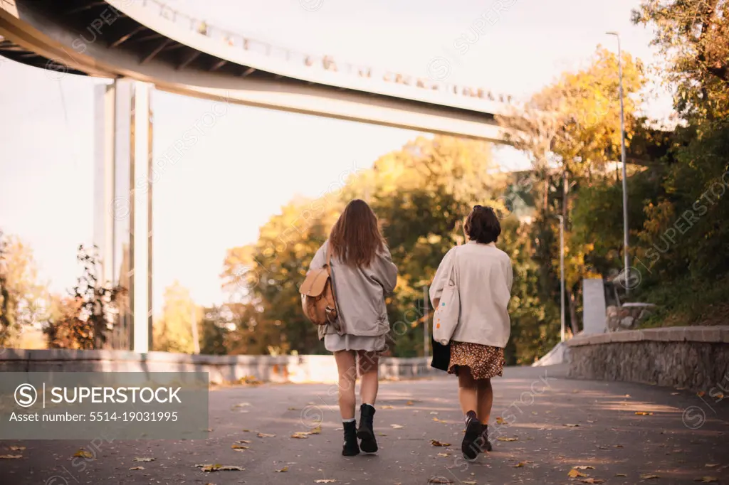 Back view of two teenage girls walking in park in city in autumn