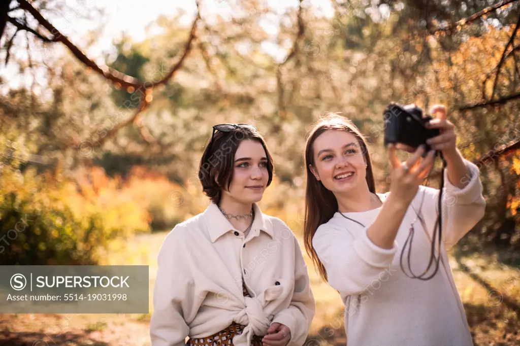Happy female friends taking selfie standing in park in autumn