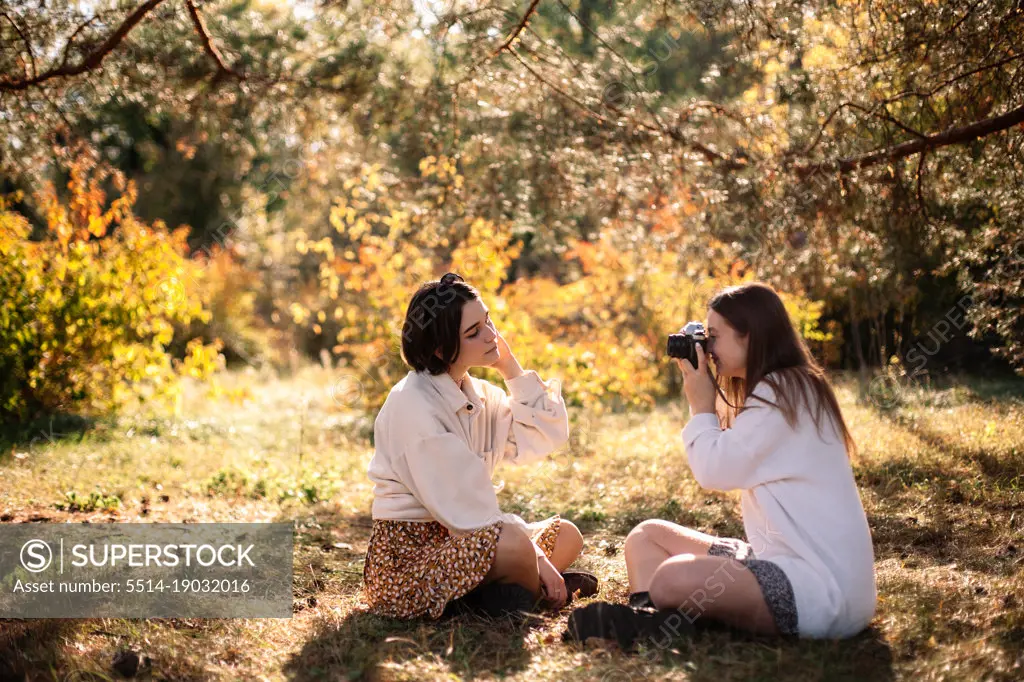 Young woman photographing girlfriend in park during autumn