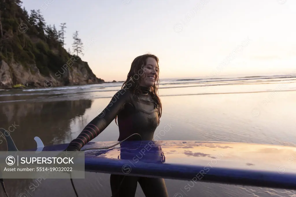 Woman carrying surfboard along beach at Short Sands, Oregon