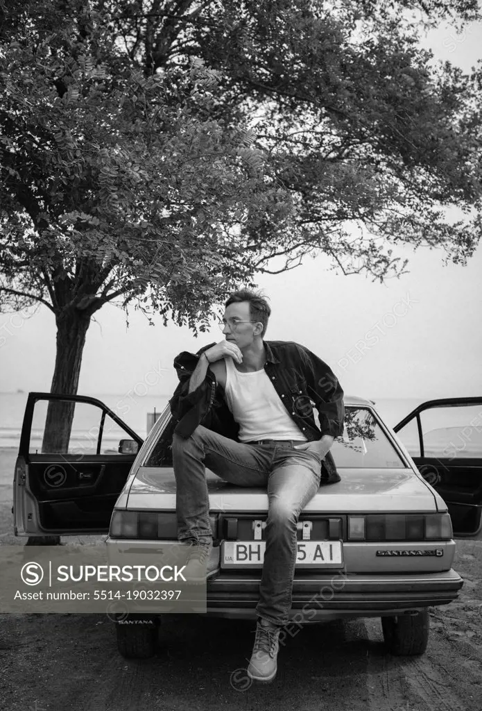 handsome man in glasses near car and tree black and white