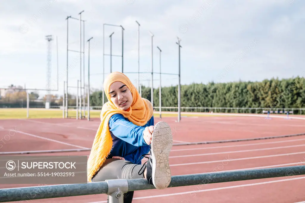 Arab woman stretching legs in stadium during workout