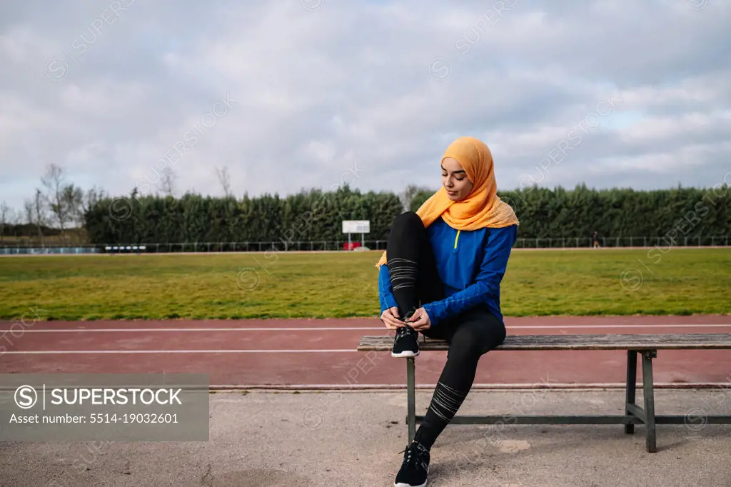 Ethnic woman sitting on bench and tying sneakers before running