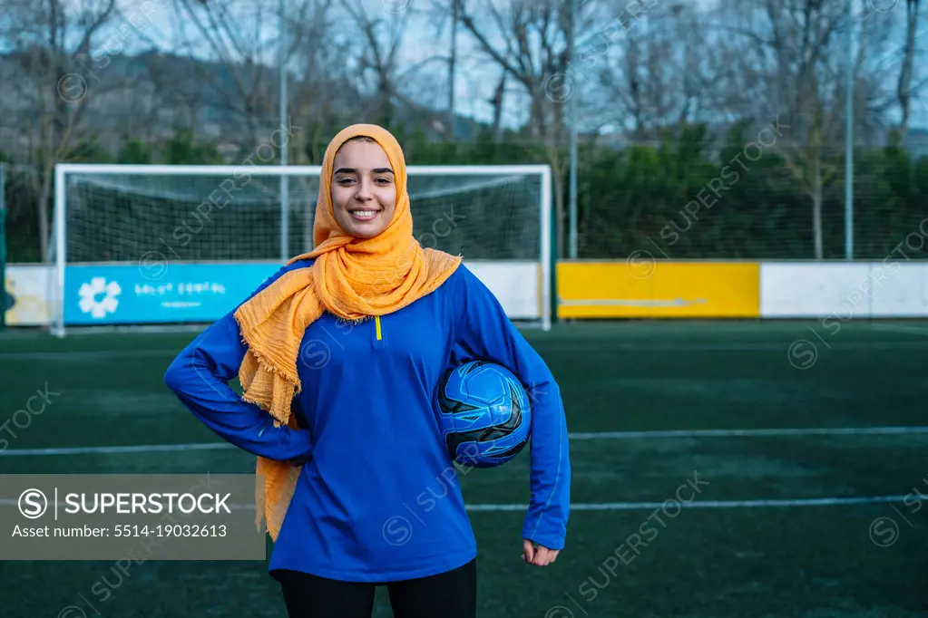 Smiling ethnic woman with football ball on sports field