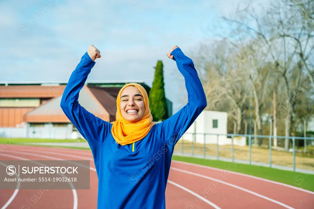 Joyful ethnic woman raising hands up and celebrating sport achievement