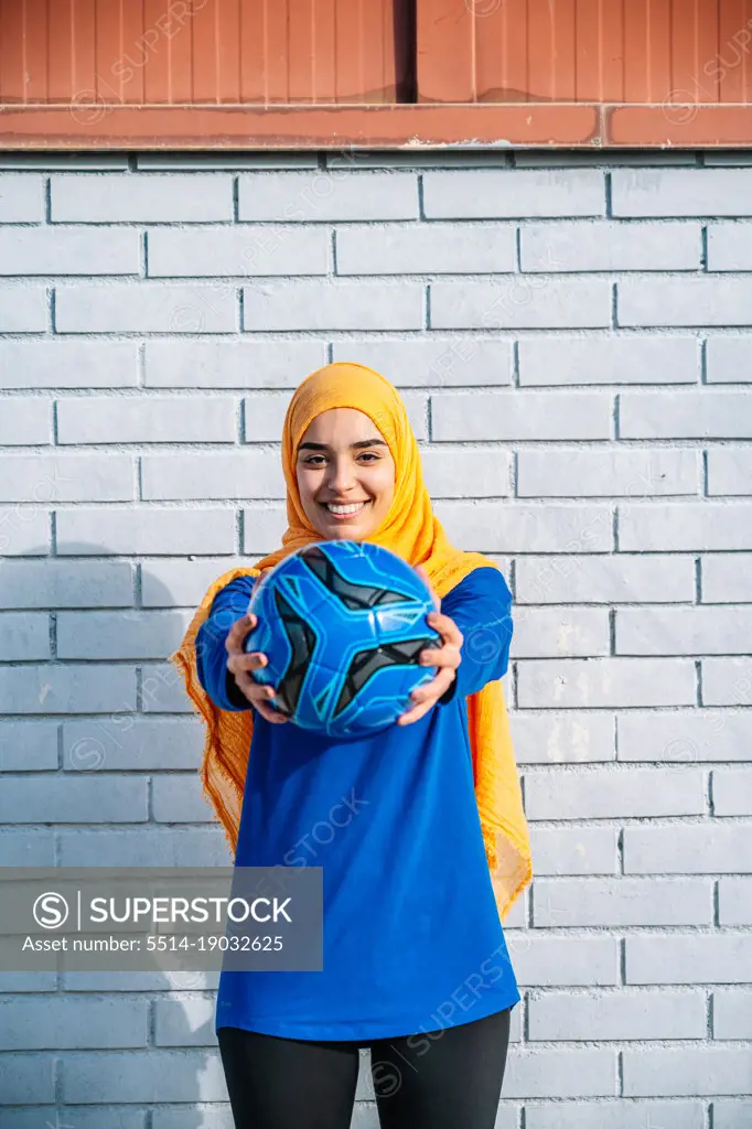 Smiling Arab female outstretching hands with ball