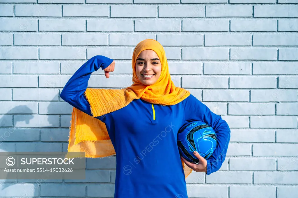 Happy ethnic woman with soccer ball showing power gesture